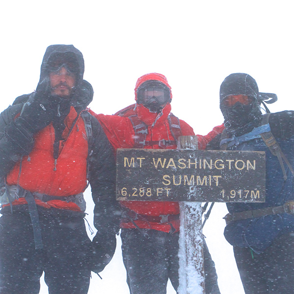 Three men standing atop Mount Washington in a snow storm